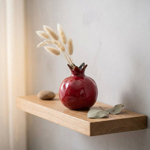 Vase grenade en céramique rouge sur une étagère en bois avec pampas séchés