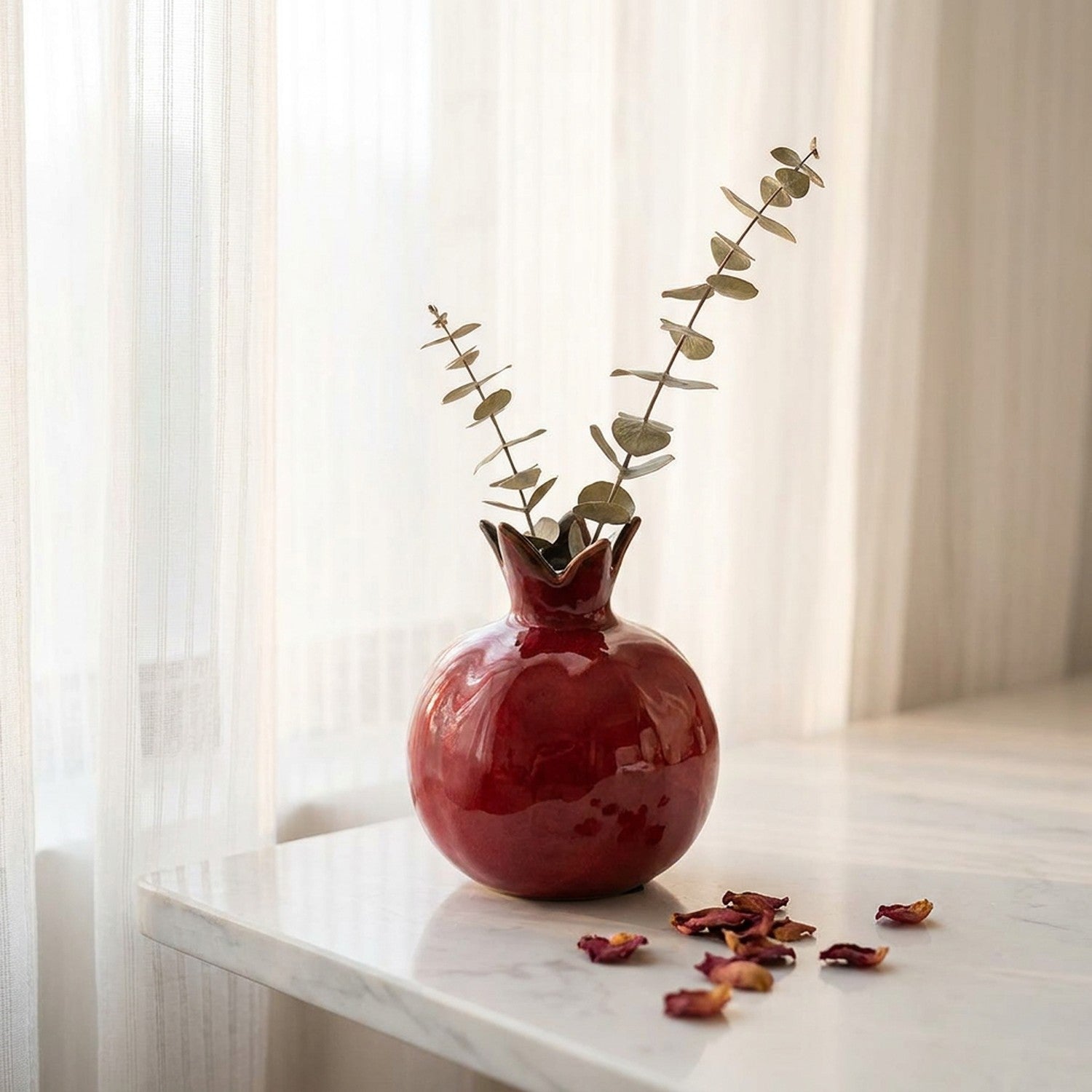 Vase grenade en céramique rouge sur une surface en marbre avec eucalyptus