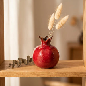 Vase en forme de grenade en céramique rouge brillante sur une étagère avec branches séchées