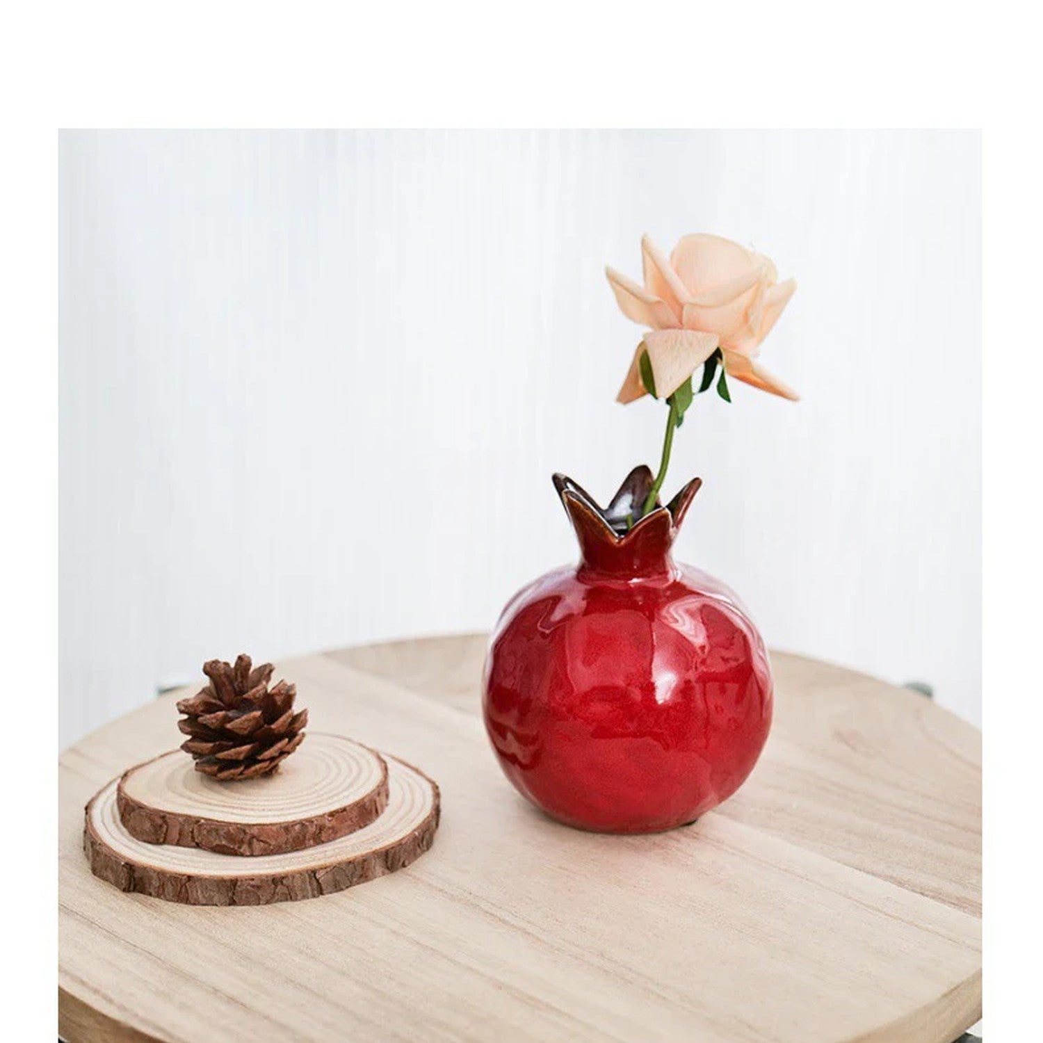 Vase grenade en céramique rouge avec une rose sur une table en bois