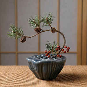 Vase Ikebana lotus en céramique couleur bleu gris avec branche de pin et baies rouges