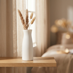 Vase blanc strié sur une étagère dans une chambre lumineuse avec des pampas