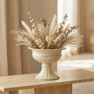 Vase médicis vintage en métal crème et doré garni d'eucalyptus séché sur une table de réception lumineuse
