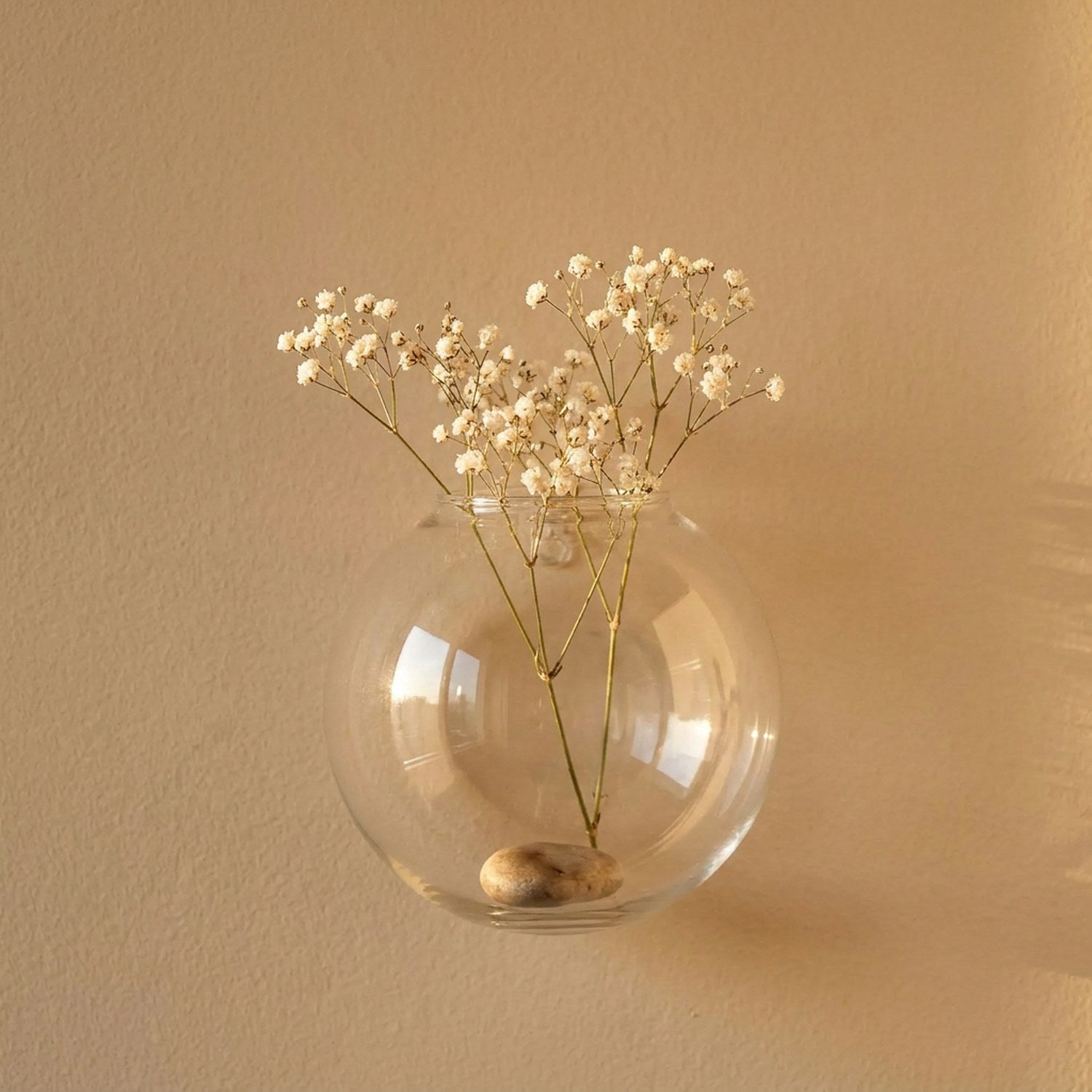 Petit vase mural en verre avec gypsophile sur mur sable doux