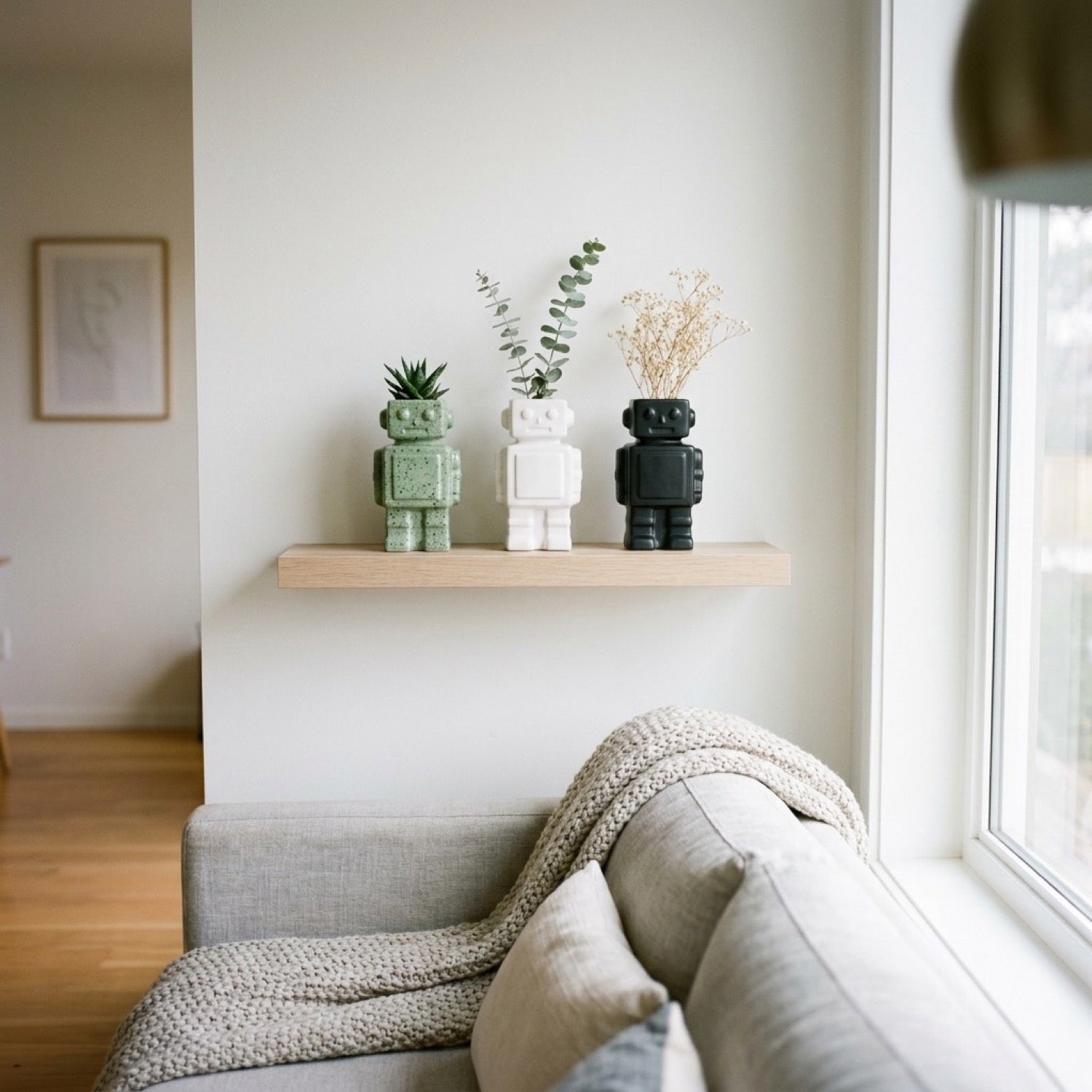 Trois vases robot alignés sur étagère flottante avec plantes dans salon scandinave