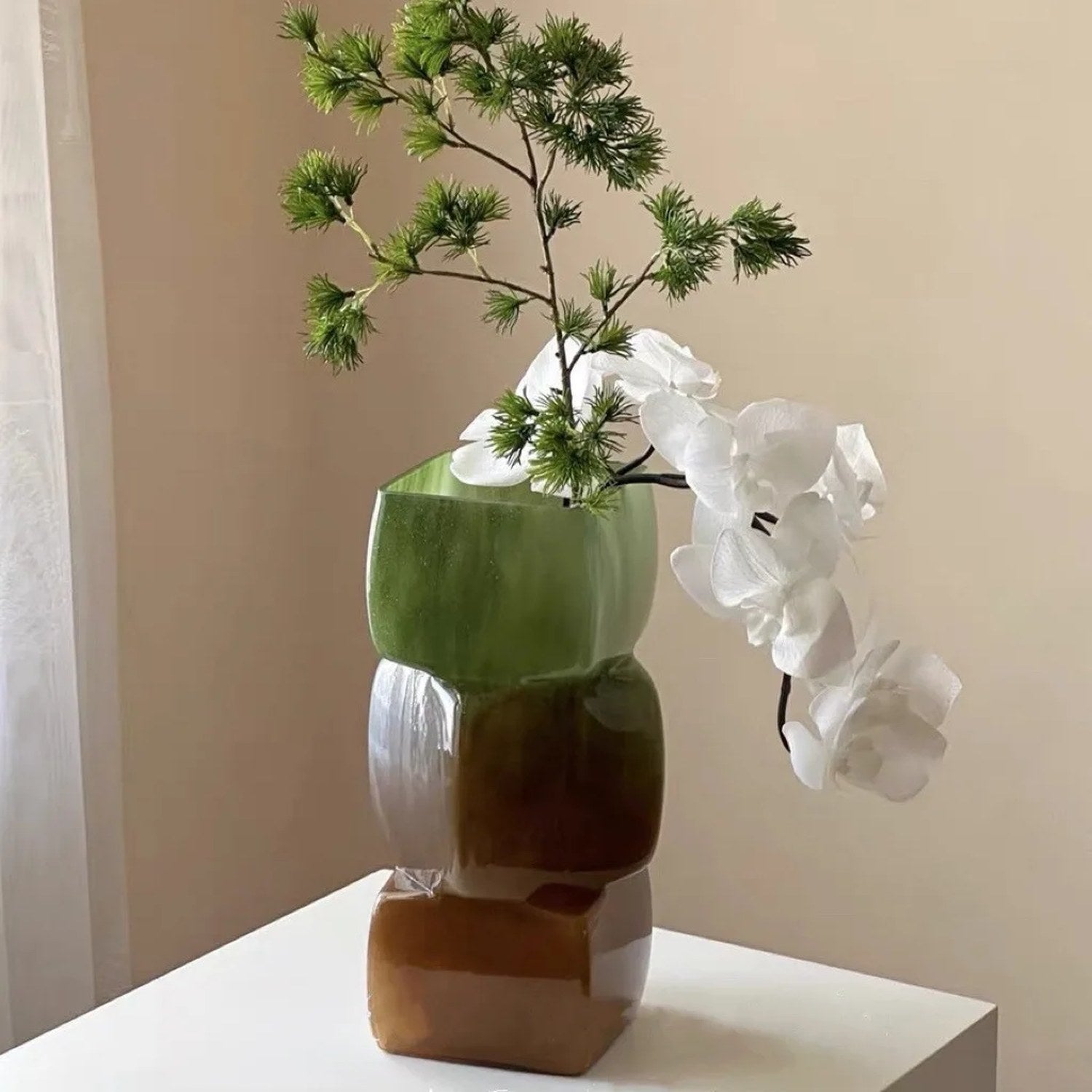 Vase géométrique vert et ambré avec orchidées et branche de pin
