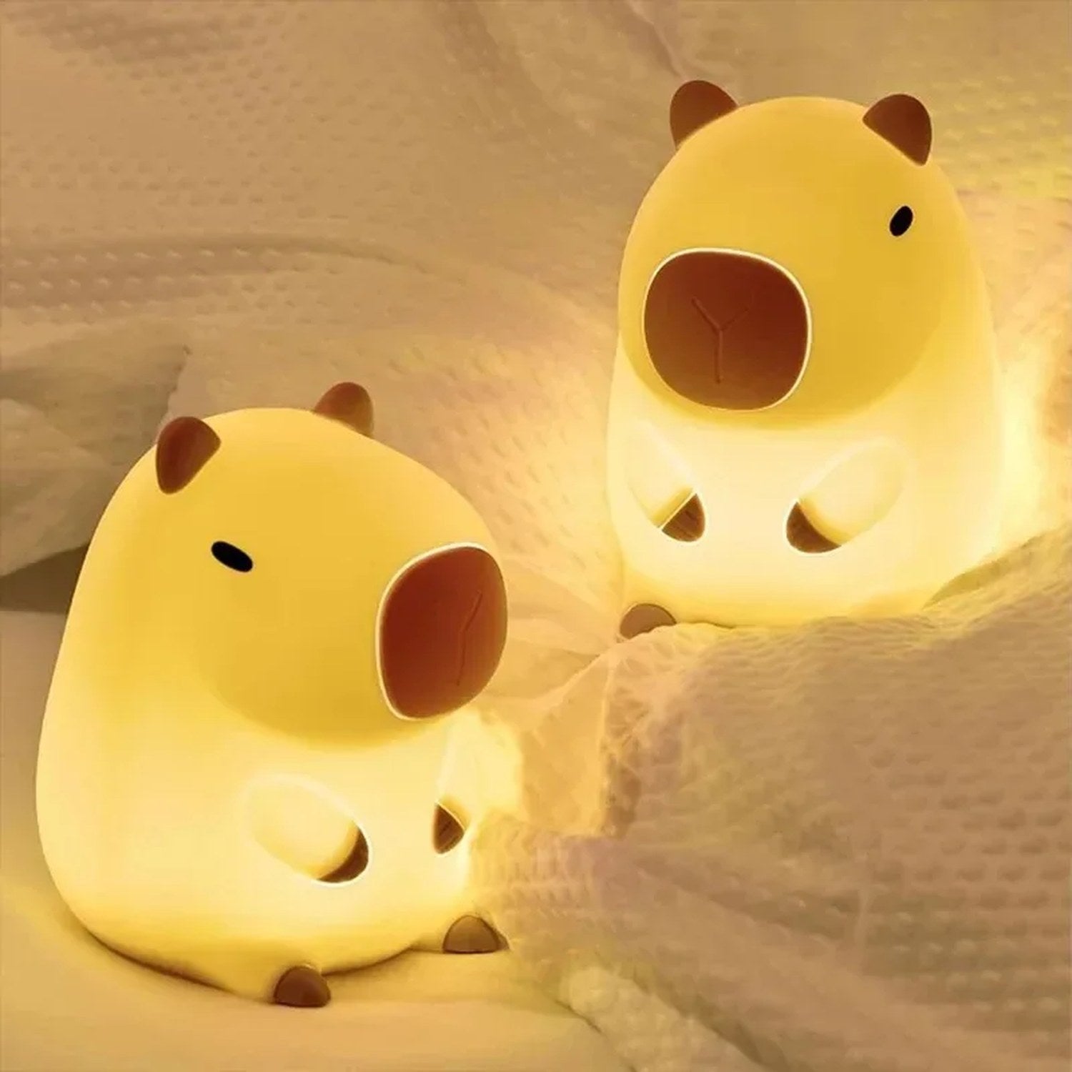 Deux veilleuses capybara allumées posées sur un plaid moelleux