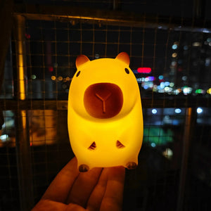 Veilleuse capybara allumée tenue dans une main la nuit