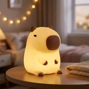 Veilleuse capybara jaune en silicone allumée posée sur une table de chevet en bois