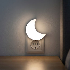 Veilleuse lune LED blanche allumée branchée sur une prise murale dans une chambre sombre