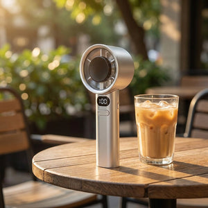 Ventilateur portable à main sur une table de terrasse à côté d'une boisson fraîche