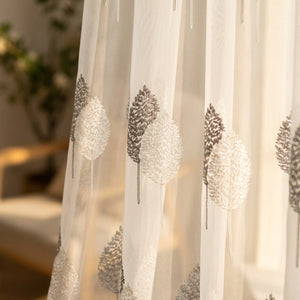 Détail du motif d'arbres brodé en fils blancs et gris sur le tulle translucide