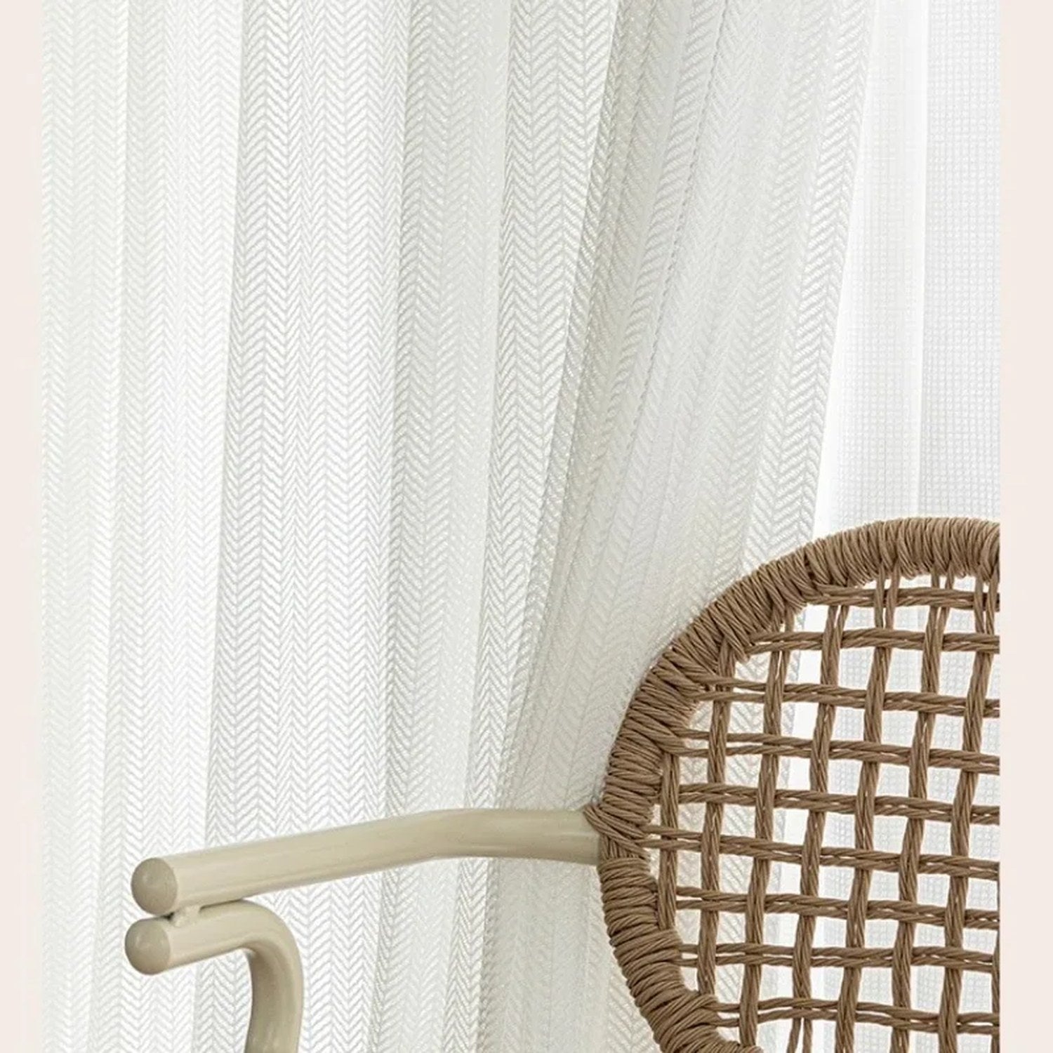 Détail du voilage tulle blanc à texture chevron dans un intérieur avec fauteuil en rotin