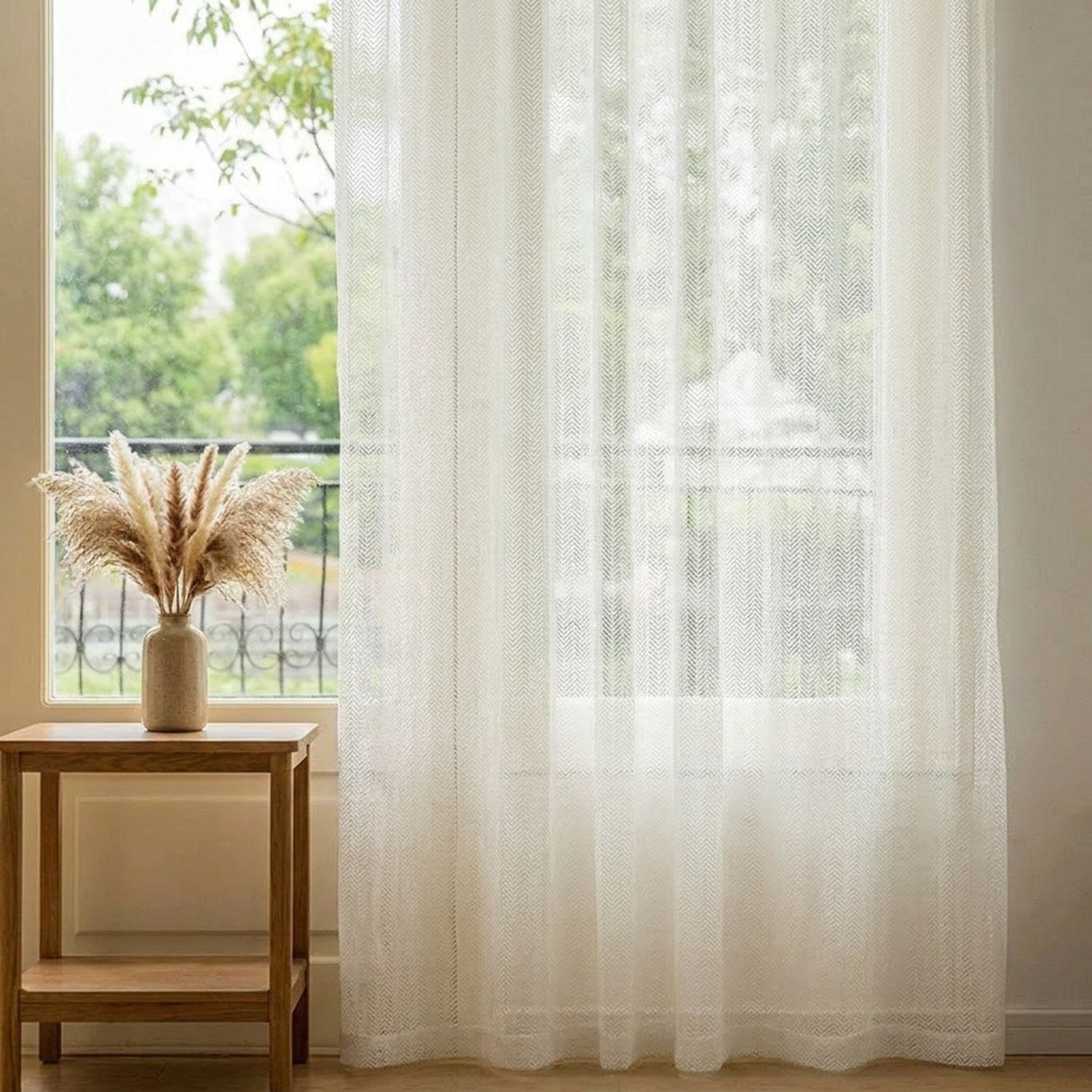 Voilage blanc à motif os de poisson devant une fenêtre avec petite table en bois et pampa