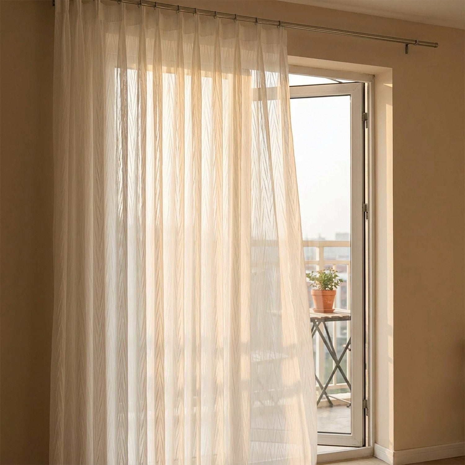Voilage blanc suspendu devant une porte fenêtre donnant sur un balcon au coucher du soleil