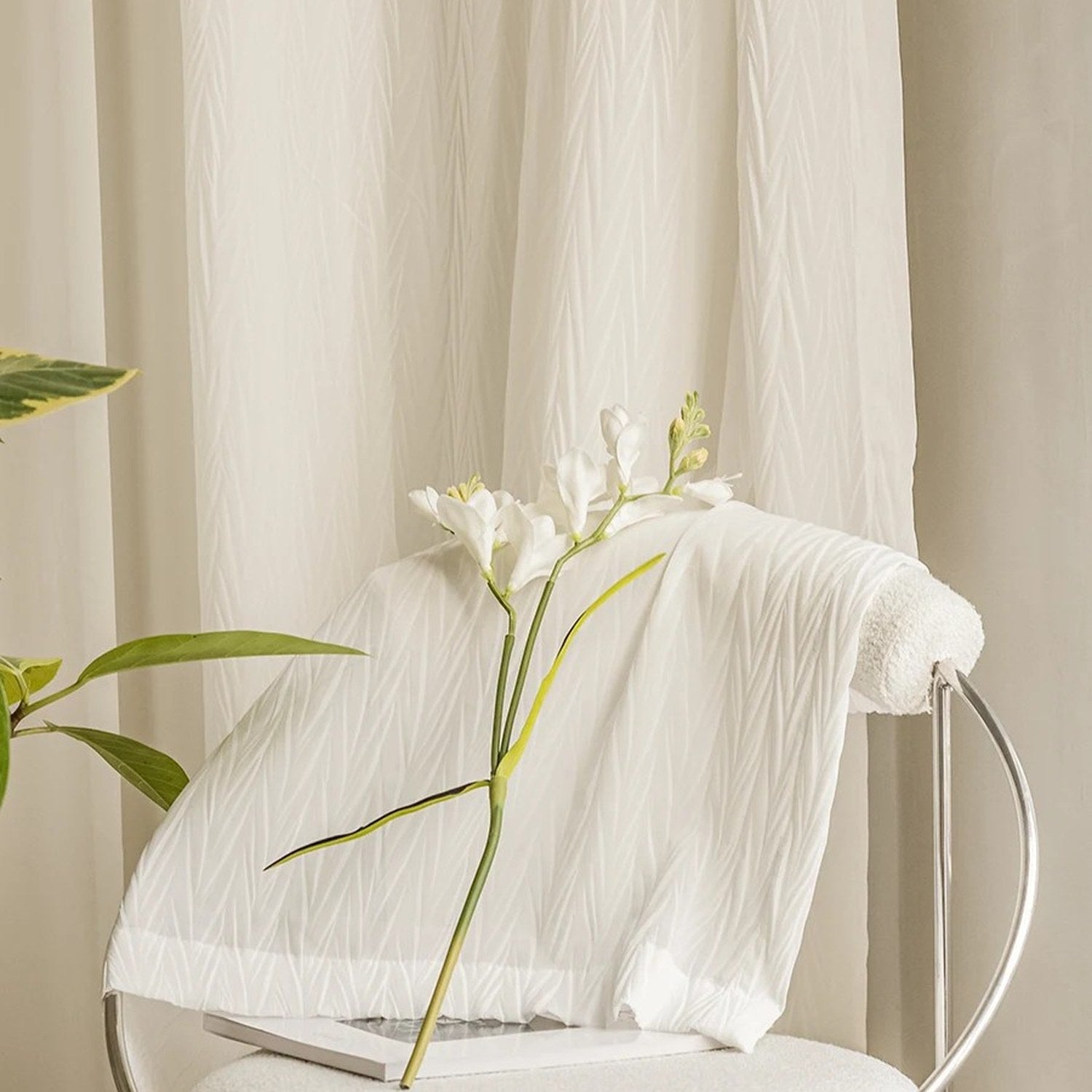 Tissu plissé blanc drapé sur une chaise devant un voilage suspendu et une fleur