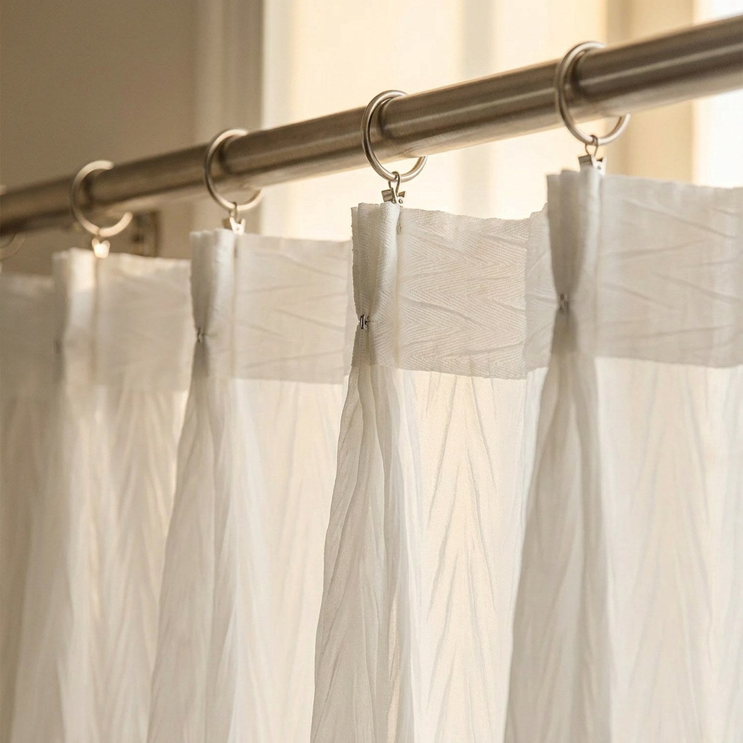 Gros plan sur la fixation à crochets du voilage plissé blanc sur une tringle