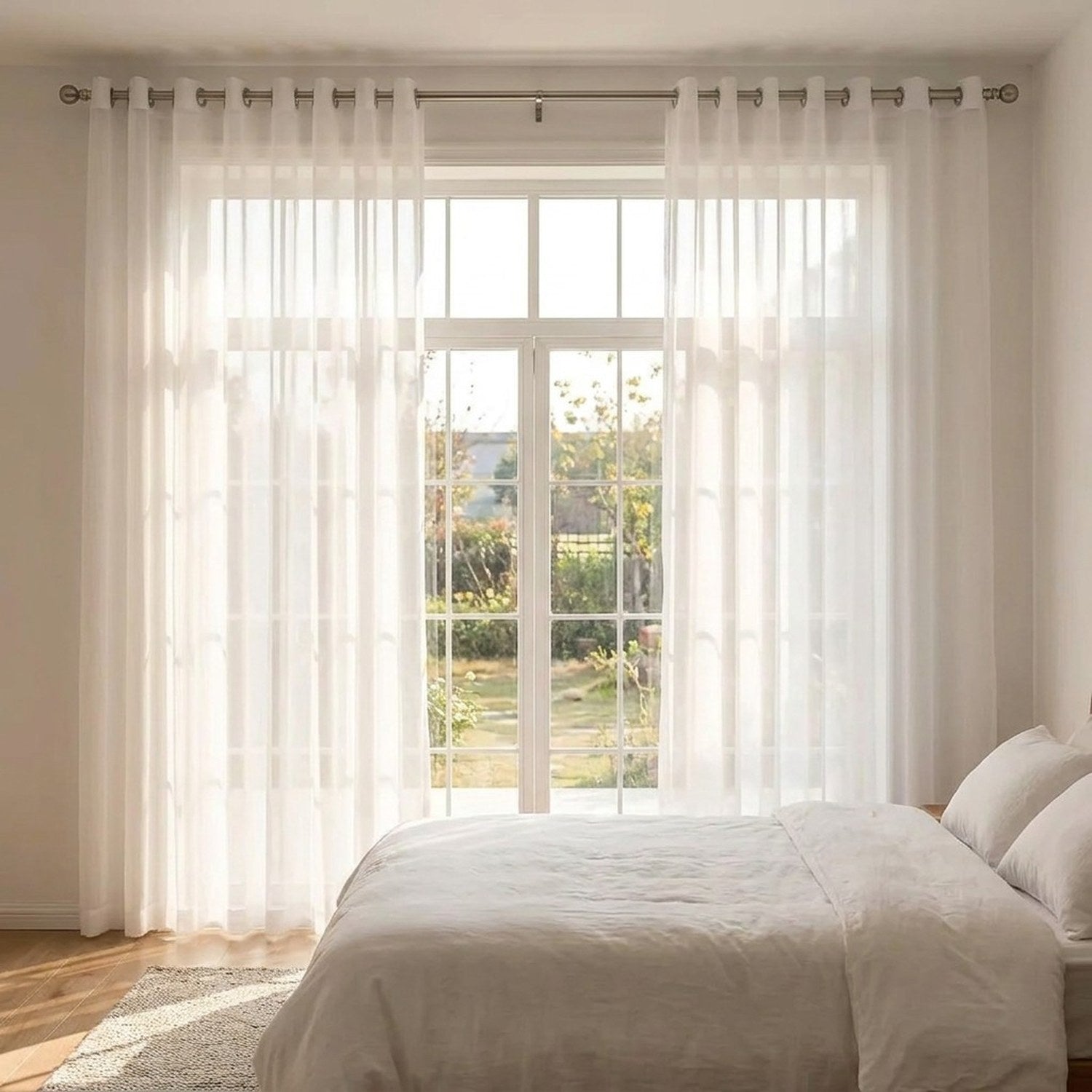 Voilage blanc encadrant une baie vitrée dans une chambre lumineuse avec lit blanc