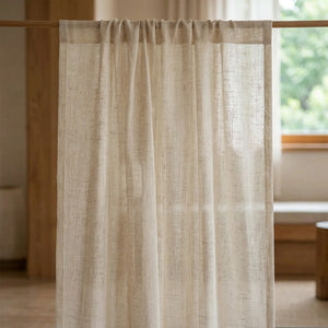 Voilage tamisant à l'aspect lin naturel de teinte écru suspendu à une fenêtre dans une chambre lumineuse et chaleureuse