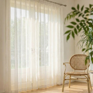 Voilage blanc à texture chevron dans un salon lumineux avec fauteuil en rotin et plante verte